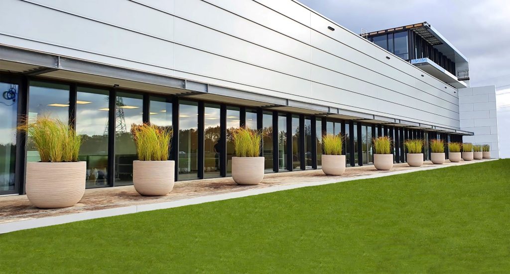Buitenshowroom met hoge geribbelde plantenbakken — Ecriliving.nl.